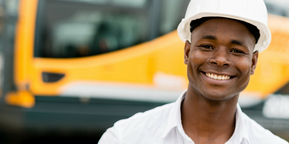 Residential Construction and Carpentry- Male Construction worker with white hard hat on in front of a yellow piece of equipment