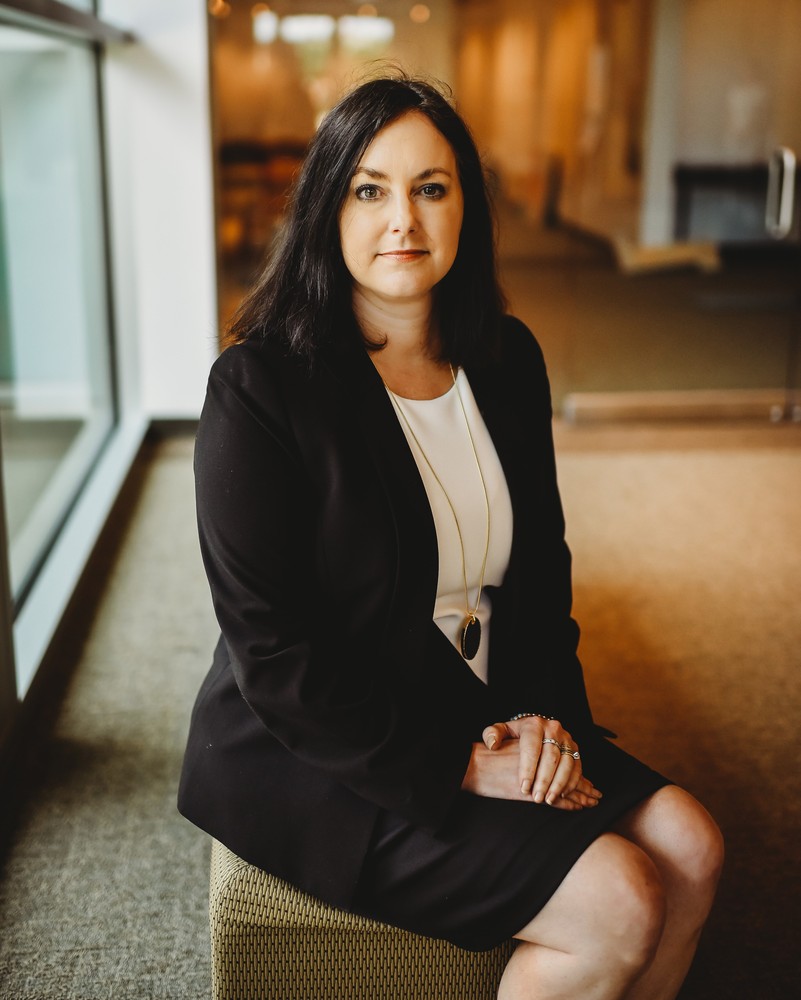 Dr. Cathie Cline sitting in the Fine Arts Center lobby in a black suit