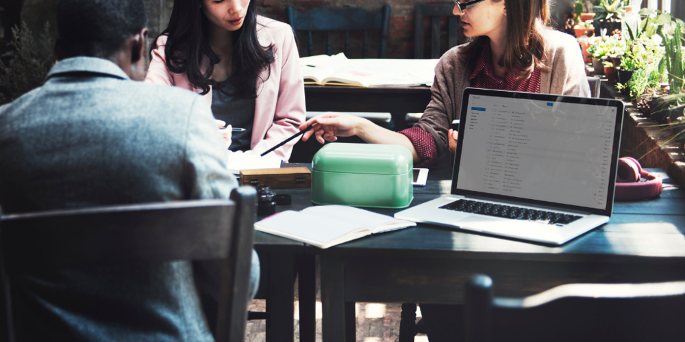 Business- two females and a male sitting at a table talking with a computer open